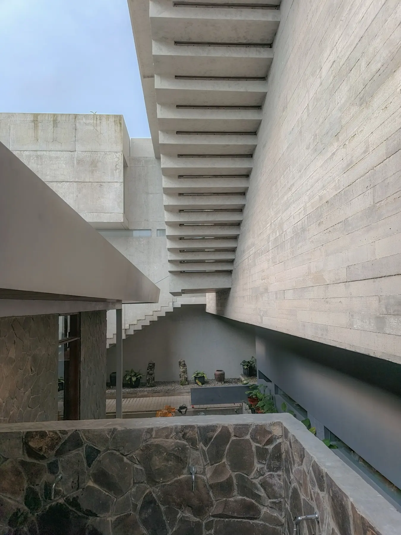 Exposed concrete eaves meeting a rough stone wall above a courtyard.